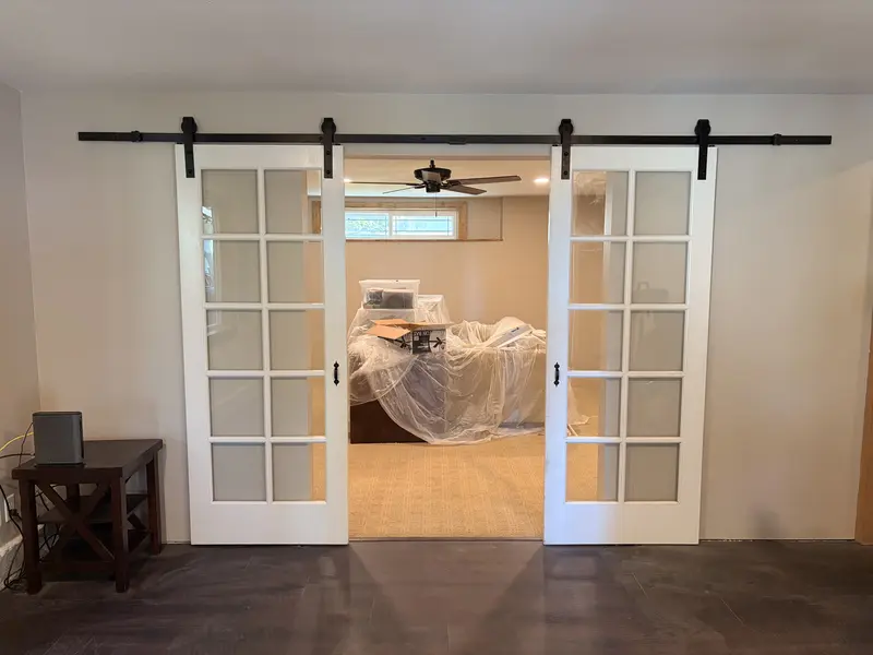 Finished room with a pair of white glass-panel barn doors opening onto a seating area, new dark flooring and stained window trim