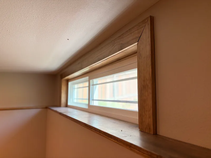 The same basement window framed with stained wood trim and a wood sill