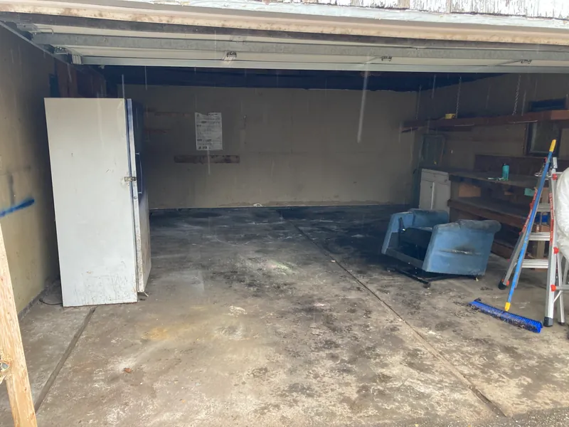 Cleared garage with a bare concrete floor, a standing refrigerator and a ladder