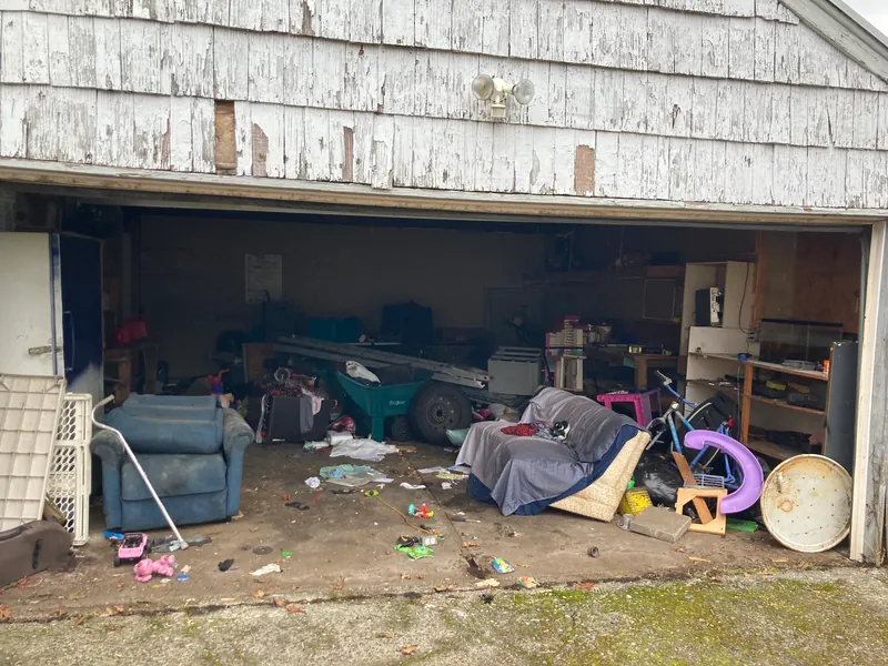 Garage packed with furniture, toys, a wheelbarrow and debris before cleanout