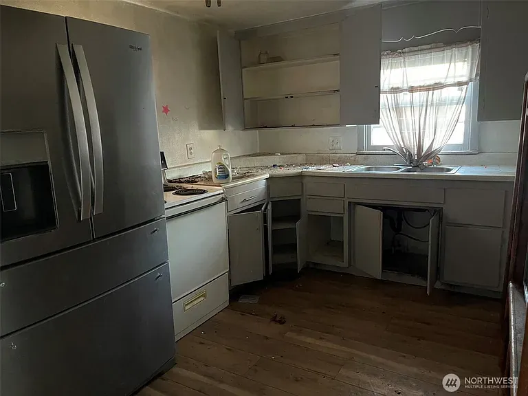 Cleared kitchen with the refrigerator, open cabinets and a clean wood floor