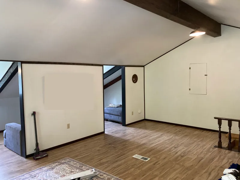 Remodeled loft with a dark wood box beam, new plank flooring and fresh white walls