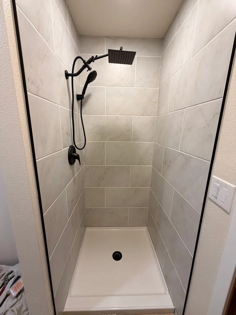Rebuilt shower with large-format marble-look tile, black fixtures and a new pan