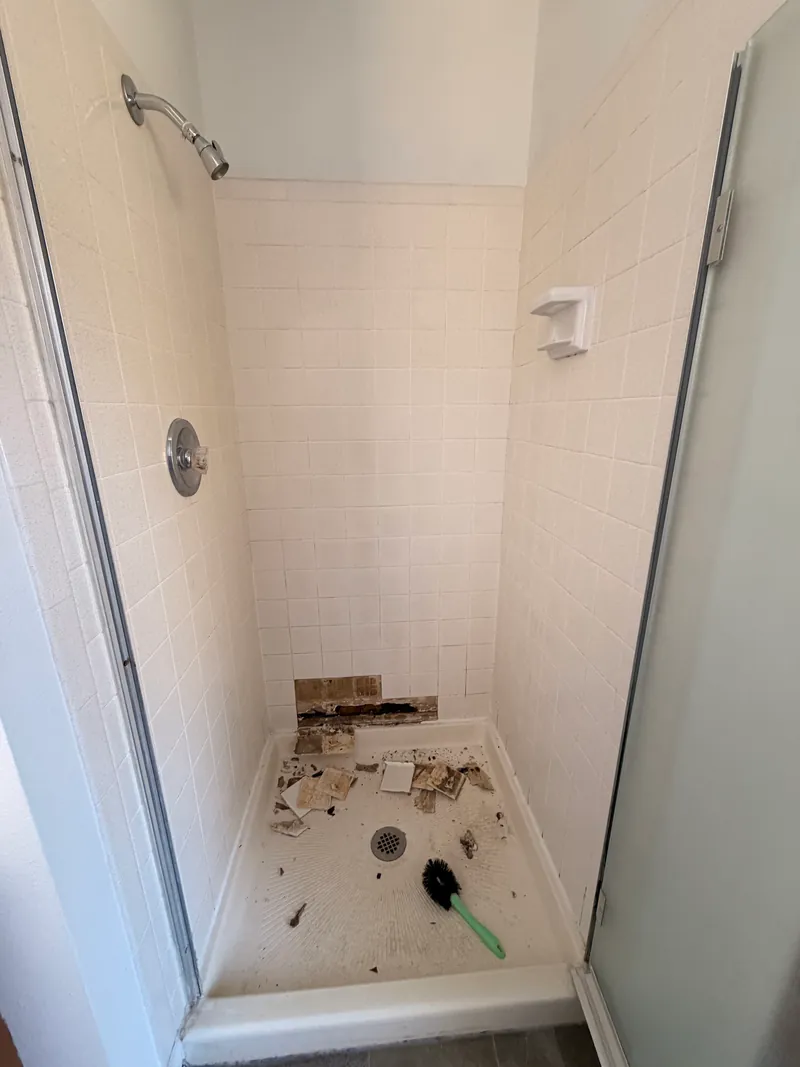 Shower with old tile and a rotted section of wall and floor opened up