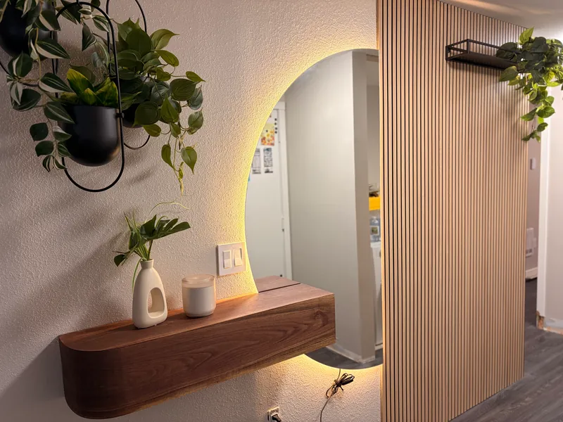 Entryway with a vertical wood slat wall, a backlit round mirror and a floating walnut shelf