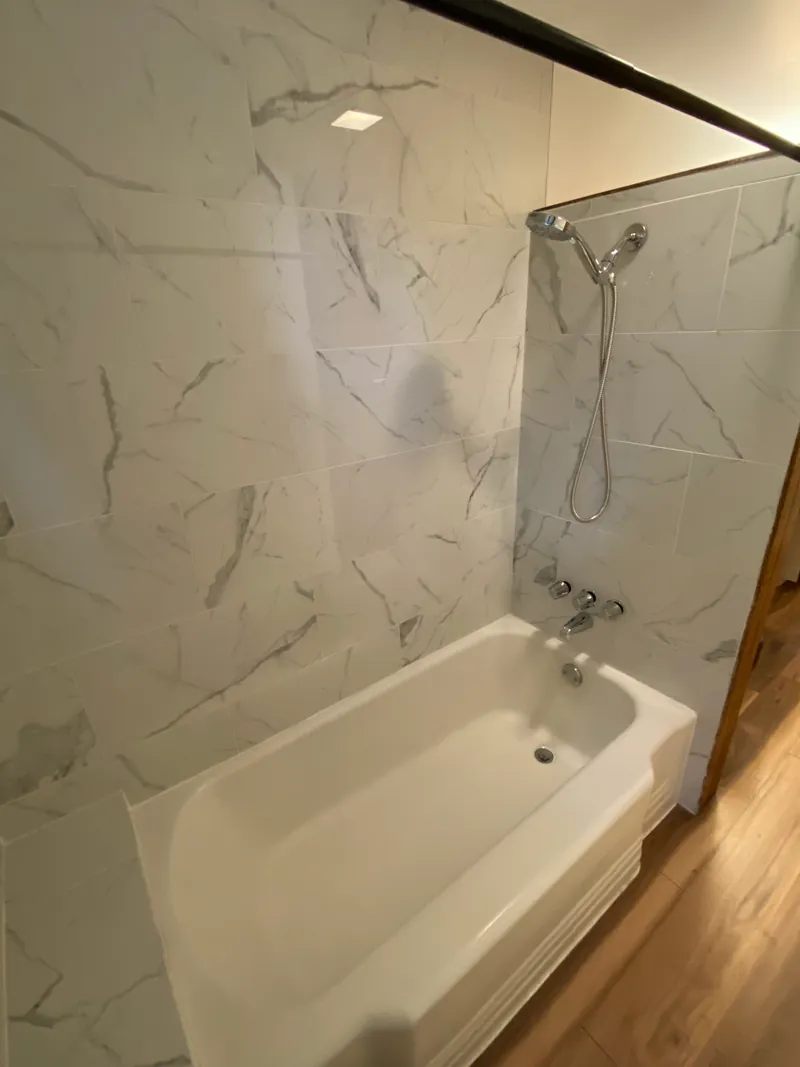 Remodeled tub and shower with large marble-look tile, a new shower fixture and new flooring