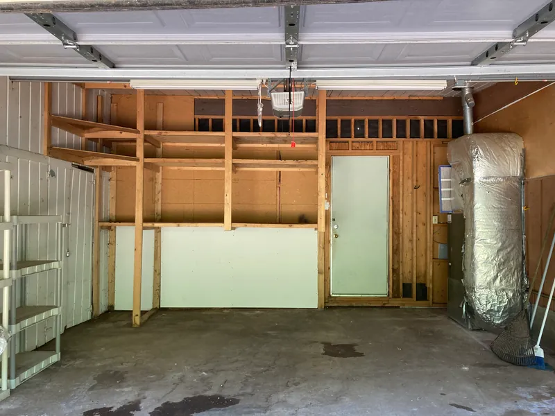 Cleared garage with exposed wall framing, a door and an insulated water heater