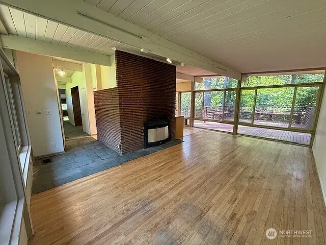 Cleared living area with a brick fireplace, hardwood floor and a wall of windows onto the trees