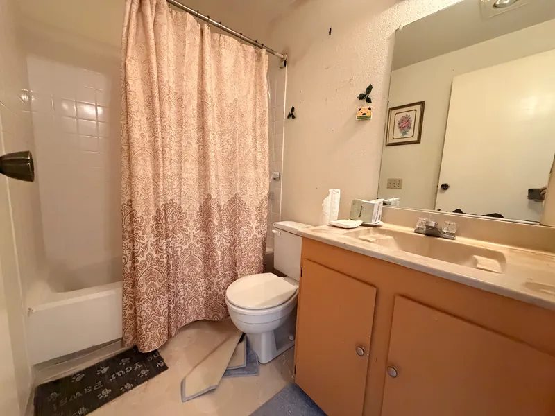 Bathroom with tub, shower curtain, tan vanity and worn flooring before renovation