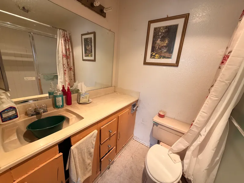 Bathroom vanity with a beige countertop, wood cabinets and a shower curtain before renovation