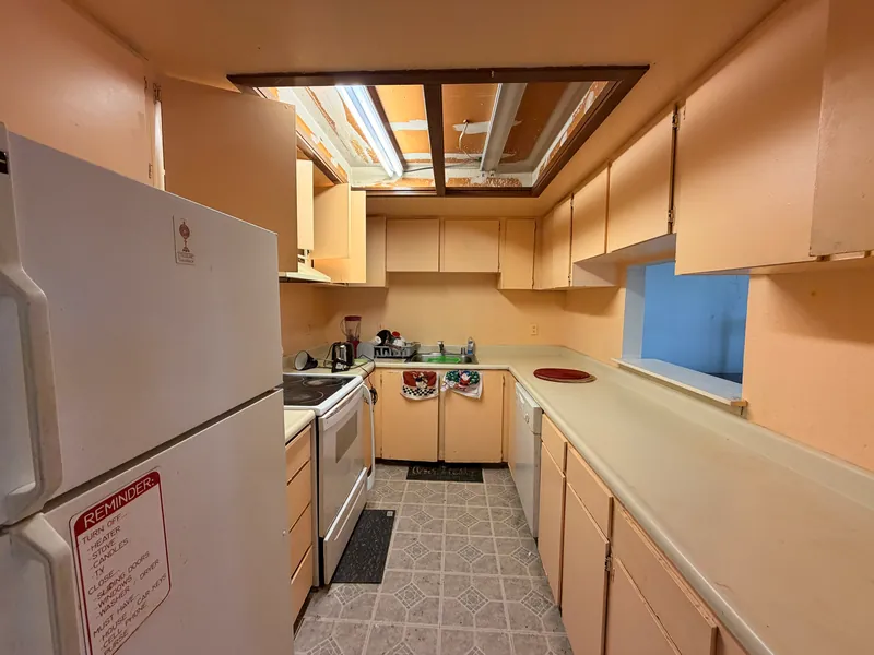 Narrow galley kitchen with tan cabinets, laminate counters and vinyl flooring before renovation