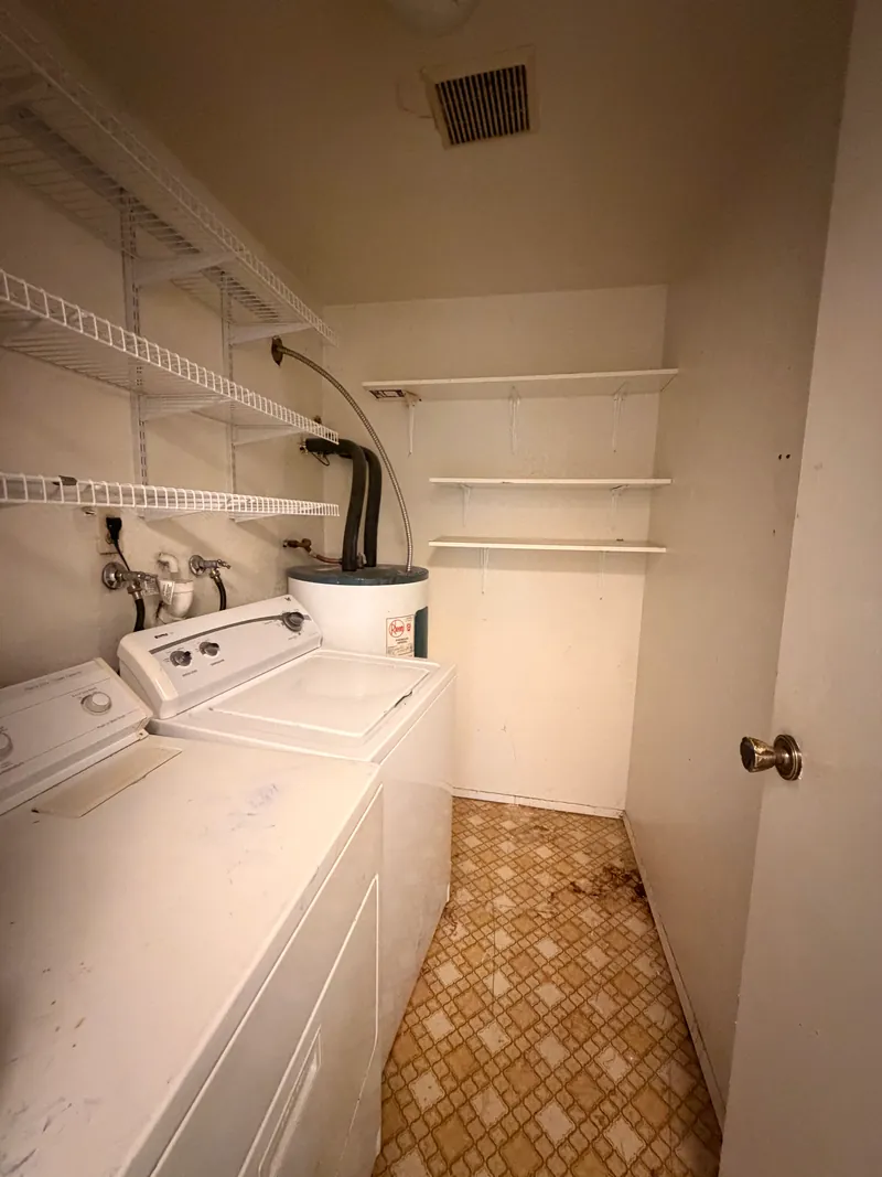 Laundry closet with washer, dryer and worn patterned vinyl flooring before renovation