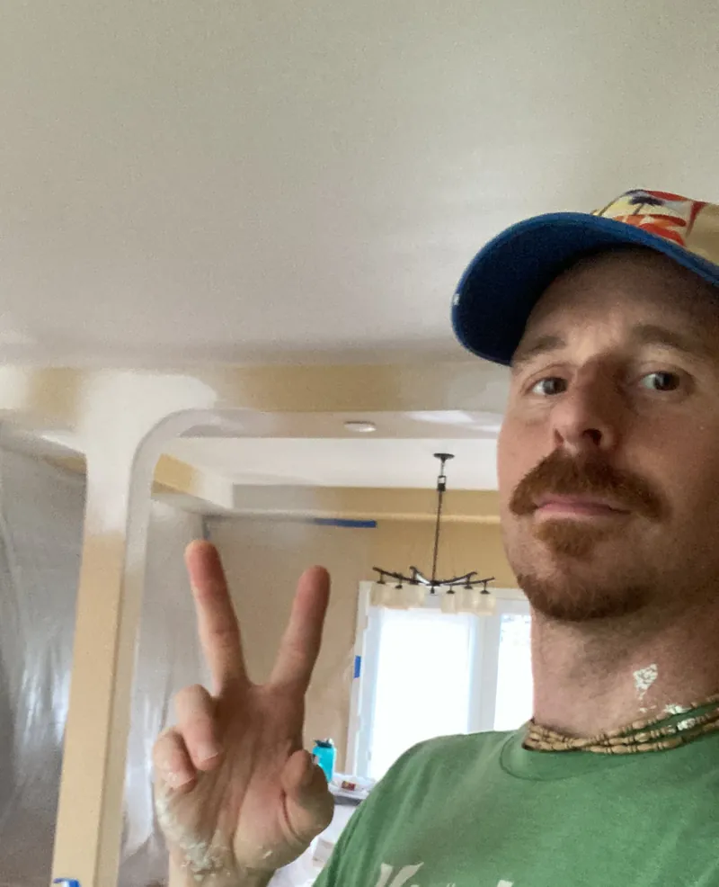 Bryant Hanahan in a cap and green T-shirt flashing a peace sign inside a room covered in protective plastic
