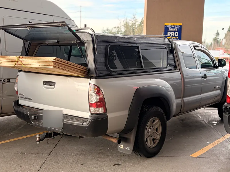 Silver Toyota Tacoma with a black canopy and a stack of lumber sticking out of the open back